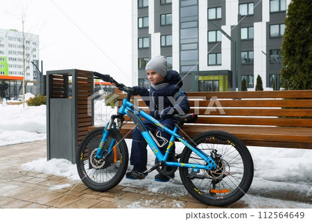 European boy dressed in a winter jacket is tired of riding a bicycle 112564649