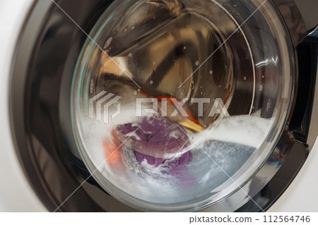 Closeup of washing machine door with spinning laundry Closeup of washing machine door with spinning laundry 112564746