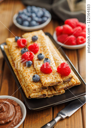 Delicate crepes stacked with blueberries and raspberries, served with a chocolate spread. Delicate crepes stacked with blueberries and raspberries, served with a chocolate spread. 112564883