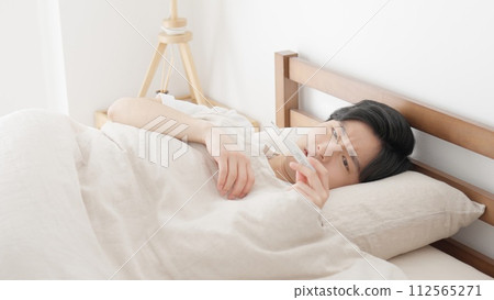 A man measures his temperature with a thermometer while sleeping A man measures his temperature with a thermometer while sleeping 112565271