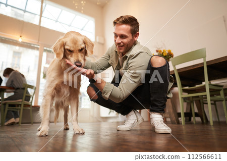 Close up portrait of happy dog owner, man with his pet giving a treat, spending time in animal-friendly cafe or co-working space Close up portrait of happy dog owner, man with his pet giving a treat, spending time in animal-friendly cafe or co-working space 112566611