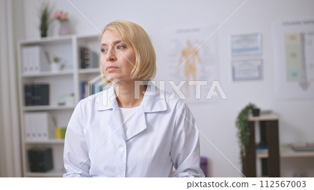 A blonde woman therapist contemplates a patient's diagnosis, providing professional health care services A blonde woman therapist contemplates a patient's diagnosis, providing professional health care services 112567003