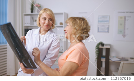 A traumatologist and a senior patient review an X-ray image, focusing on recovery after trauma A traumatologist and a senior patient review an X-ray image, focusing on recovery after trauma 112567016
