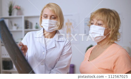 A physiatrist and a patient in medical masks talk over an MRI scan, concentrating on rehabilitation 112567025