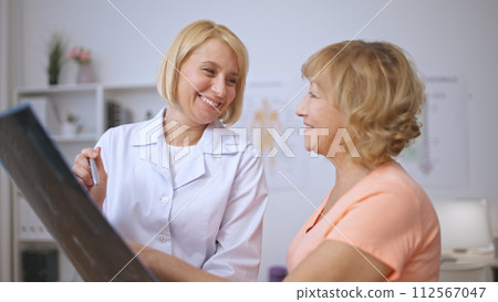 A happy senior patient and a kind female doctor discuss an X-ray image and share a smile A happy senior patient and a kind female doctor discuss an X-ray image and share a smile 112567047