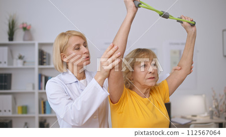 A rehabilitation center doctor assists a senior patient with muscle-strengthening exercises A rehabilitation center doctor assists a senior patient with muscle-strengthening exercises 112567064