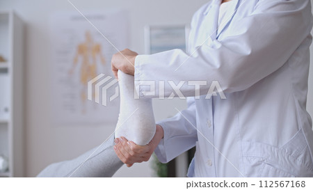 A traumatologist facilitates a patient's foot exercise, focusing on rehabilitation after a sports injury A traumatologist facilitates a patient's foot exercise, focusing on rehabilitation after a sports injury 112567168