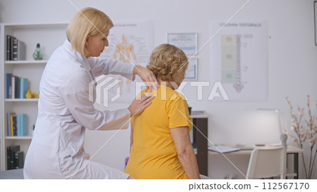 A vertebrology clinic doctor examines a senior patient's spine, conducting disease diagnostics 112567170