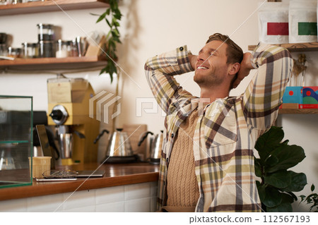 Portrait of man doing big stretch with satisfied smile, finishing his project, sitting in cafe with laptop and phone, drinking coffee Portrait of man doing big stretch with satisfied smile, finishing his project, sitting in cafe with laptop and phone, drinking coffee 112567193
