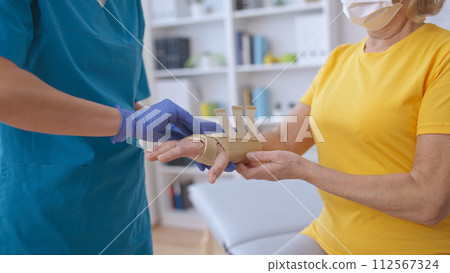 A medical worker examines a senior female patient's injured arm in a band, treating a sprain 112567324