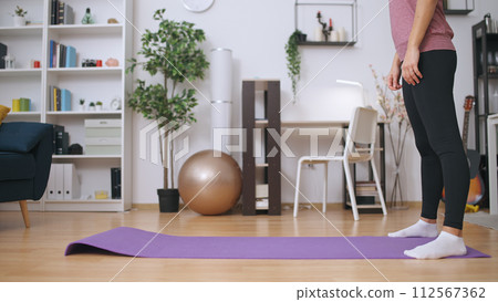 A woman prepares to do yoga and stretching exercises on a fitness mat at home, promoting a healthy lifestyle A woman prepares to do yoga and stretching exercises on a fitness mat at home, promoting a healthy lifestyle 112567362