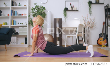 A middle-aged woman performs yoga and stretching exercises at home, leading a healthy lifestyle 112567363