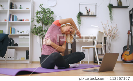 A beautiful fit woman trains at home, watching an online tutorial on her laptop, dedicated to fitness 112567367