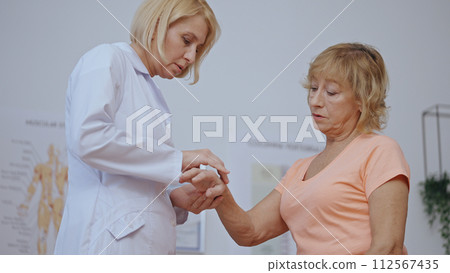 A woman orthopedist examines a mature lady's injured hand, checking the recovery process 112567435