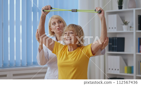 A senior woman performs exercises under a doctor's supervision, partaking in physical therapy 112567436