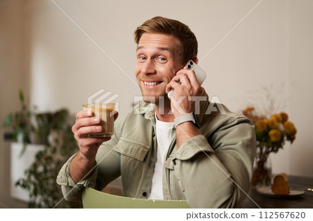 Portrait of handsome young man talking on the phone, sitting in cafe and drinking coffee, answering a call 112567620