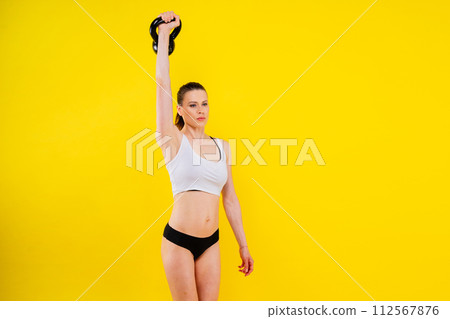Fitness female holds a kettlebell in rack position, dark yellow red background Fitness female holds a kettlebell in rack position, dark yellow red background 112567876