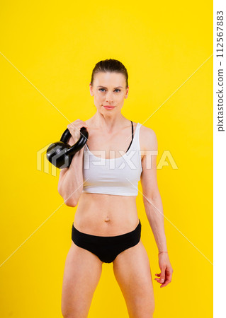 Fitness female holds a kettlebell in rack position, dark yellow red background 112567883