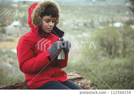 Teenage hiker traveler adventurer bot taking a break during trekking in mountains, sitting on a log in the forest Teenage hiker traveler adventurer bot taking a break during trekking in mountains, sitting on a log in the forest 112568159