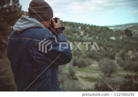 Rear view male travel photographer capturing beautiful of the mountains om his professional digital camera while hiking 112568292