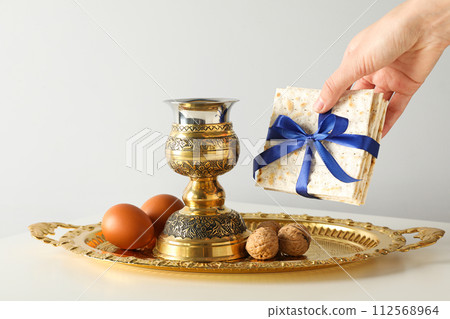 Matzo in hand, eggs, nuts and cup on tray on light background 112568964