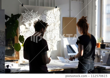 Creative duo in a sunlit studio focuses on crafting intricate paper art 112570615