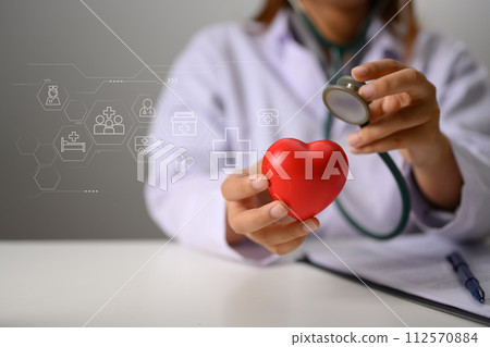 Hands of doctor holding stethoscope and red heart. Health insurance and cardiology concept Hands of doctor holding stethoscope and red heart. Health insurance and cardiology concept 112570884