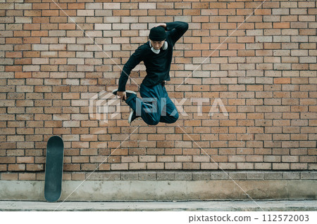 Shot of young hipster man jumping against brick wall, copy space Shot of young hipster man jumping against brick wall, copy space 112572003