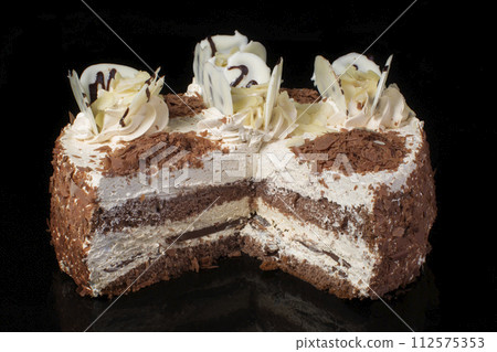Piece of white cake poured with chocolate and decorated with oil cream on a black background 112575353