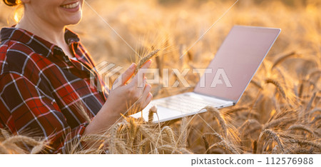 Woman farmer working with laptop on wheat field. Smart farming and digital agriculture 112576988