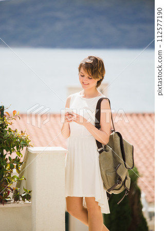 A woman holds a smartphone in her hands. Woman tourist on the street of coastal city.. A woman holds a smartphone in her hands. Woman tourist on the street of coastal city.. 112577190