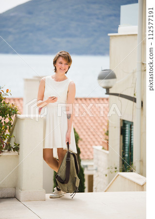 A woman holds a smartphone in her hands. Woman tourist on the street of coastal city.. A woman holds a smartphone in her hands. Woman tourist on the street of coastal city.. 112577191