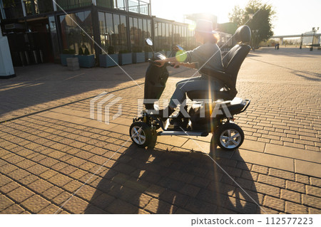 Woman tourist riding a four wheel mobility electric scooter on a city street 112577223