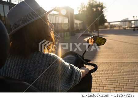 Woman tourist on a four wheel mobility electric scooter on a city street. The woman's face is visible in the rearview mirror.. 112577252