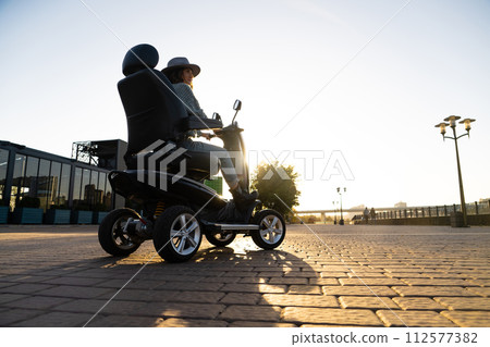 Woman tourist riding a four wheel mobility electric scooter on a city street 112577382