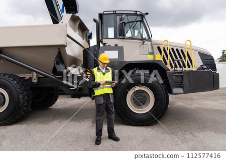 Man worker with tablet computer stands next to mining truck Man worker with tablet computer stands next to mining truck 112577416
