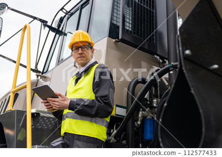 Engineer with tablet computer stands on the stairs to the cab of a truck.. 112577433