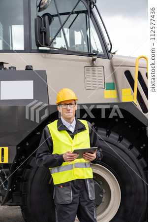 Man worker with tablet computer stands next to mining truck 112577436