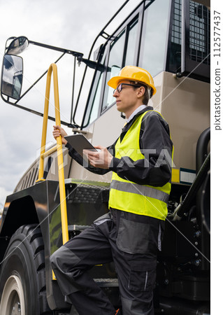 Engineer with tablet computer stands on the stairs to the cab of a truck.. 112577437