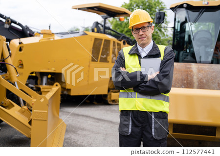 Engineer with digital tablet next to road construction machine Engineer with digital tablet next to road construction machine 112577441
