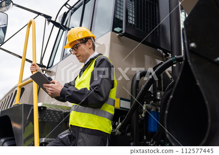 Engineer with tablet computer stands on the stairs to the cab of a truck.. Engineer with tablet computer stands on the stairs to the cab of a truck.. 112577445