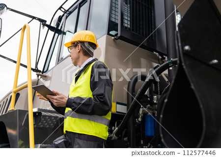 Engineer with tablet computer stands on the stairs to the cab of a truck.. 112577446