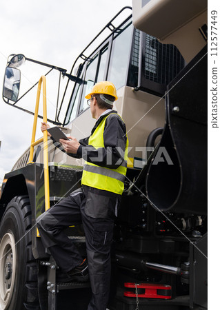 Engineer with tablet computer stands on the stairs to the cab of a truck.. 112577449
