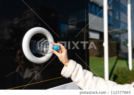 Woman uses a self service machine to receive used plastic bottles and cans on a city street.. 112577665