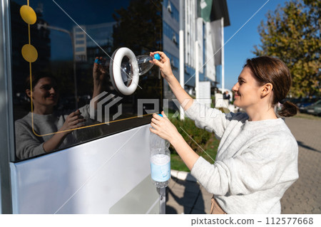 Woman uses a self service machine to receive used plastic bottles and cans on a city street.. 112577668