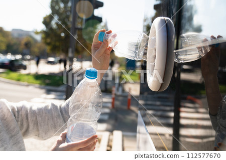 Woman uses a self service machine to receive used plastic bottles and cans on a city street.. 112577670