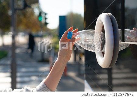 Woman uses a self service machine to receive used plastic bottles and cans on a city street.. 112577672