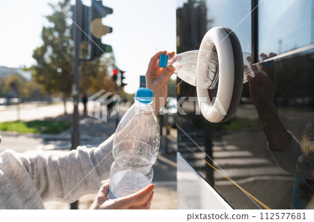 Woman uses a self service machine to receive used plastic bottles and cans on a city street.. 112577681