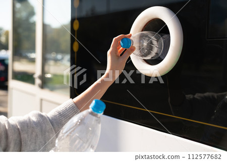 Woman uses a self service machine to receive used plastic bottles and cans on a city street.. Woman uses a self service machine to receive used plastic bottles and cans on a city street.. 112577682