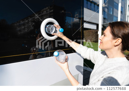 Woman uses a self service machine to receive used plastic bottles and cans on a city street.. Woman uses a self service machine to receive used plastic bottles and cans on a city street.. 112577688